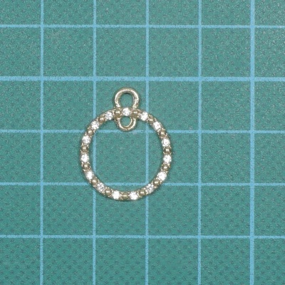 Pingente circular prateado com pedras brilhantes numa superfície verde quadriculada