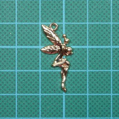 Pendente dourado em forma de fada sobre superfície verde quadriculada