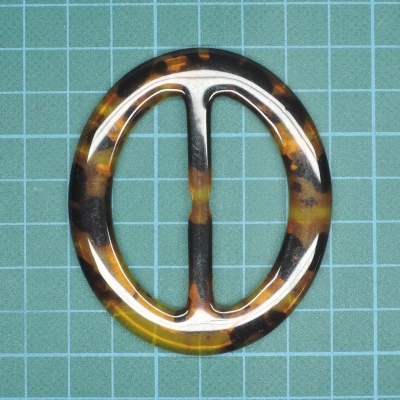 Fivela oval tigrada em plástico com barra central sobre fundo quadriculado