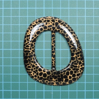 Fivela oval com padrão de pele de leopardo sobre superfície azul com grade branca