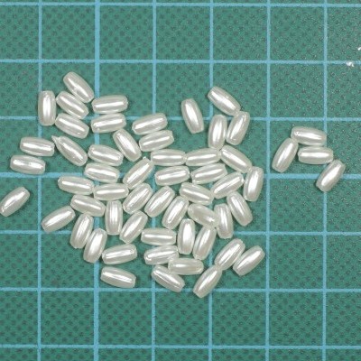 Pérolas artificiais ovais brancas sobre fundo quadriculado verde.