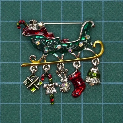 Broche metálico em forma de trenó de Natal com figuras penduradas coloridas