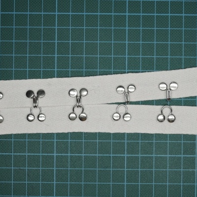 Fitas brancas com fechos metálicos prateados sobre superfície verde quadriculada