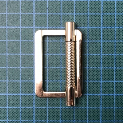 Fivela metálica dourada sobre superfície quadriculada azul e verde