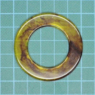 Anel circular em resina translúcida amarelo e castanho sobre superfície quadriculada verde