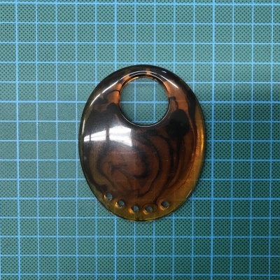 Peça oval em plástico castanho translúcido com padrão marmoreado sobre fundo quadriculado azul.