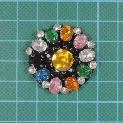 Broche redondo com pedras coloridas sobre fundo quadriculado azul