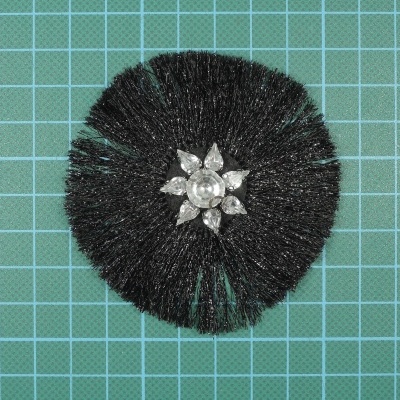 Escova redonda preta com adereço prateado em superfície quadriculada verde