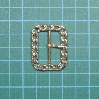 Fivela dourada retangular com corrente sobre superfície azul quadriculada