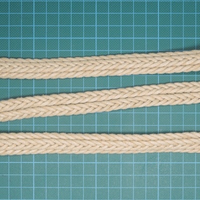 cinto trançado bege com fivela oval colocado sobre superfície quadriculada verde