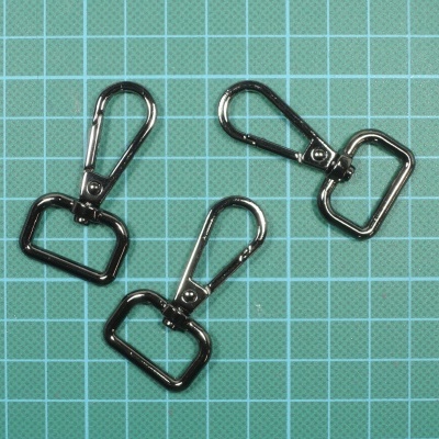 Três fechos metálicos prateados com mosquetão e anel retangular sobre fundo azul quadriculado