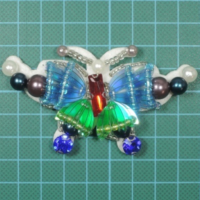 Broche borboleta com miçangas coloridas sobre superfície verde quadriculada