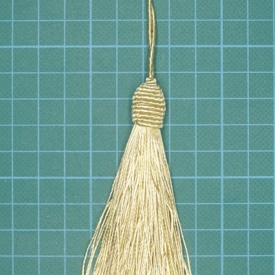 Pêndulo decorativo em bege com fios finos e argola de pendurar sobre fundo quadriculado