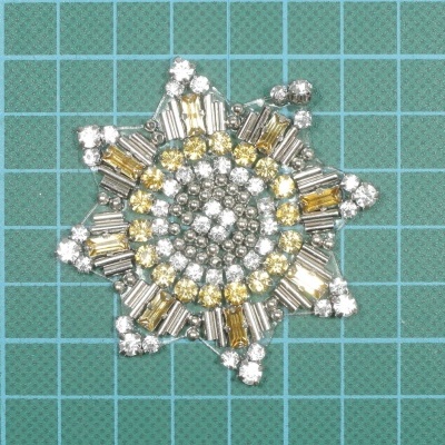 Adorno de estrela com pedras brancas e amarelas sobre fundo verde de grade azul