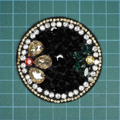 Broche redondo preto com pedras coloridas e brilhantes sobre fundo quadriculado azul