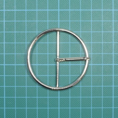 Fivela circular de metal prateado sobre superfície de corte verde com grelha branca