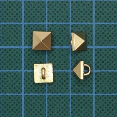 Botões metálicos dourados em formato de pirâmide quadrada sobre superfície verde quadriculada