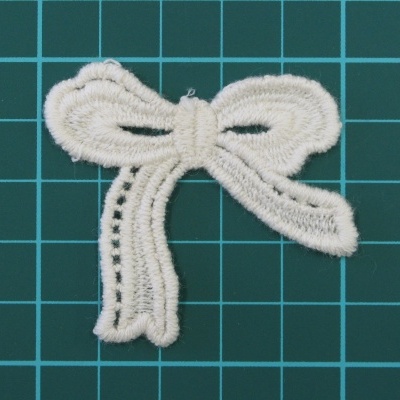 Aplicação bordada em forma de laço branco sobre fundo quadriculado verde escuro