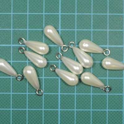 Dez contas em forma de gota cor pérola com anéis metálicos sobre superfície quadriculada azul.