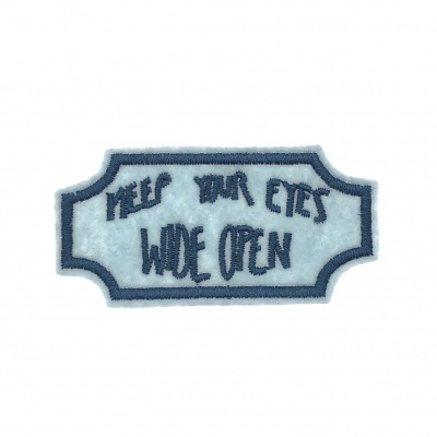 Etiqueta de tecido azul com texto bordado azul escuro 'KEEP YOUR EYES WIDE OPEN'