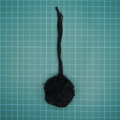 Pom pom preto com fita numa superfície quadriculada verde