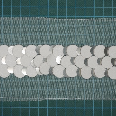 Faixa de tecido transparente com lantejoulas prateadas sobre fundo quadriculado verde