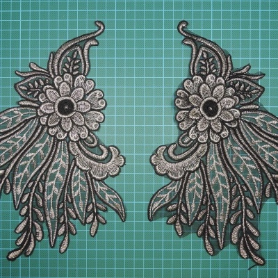 Par de apliques florais bordados em tecido preto e cinza sobre superfície verde com grade branca