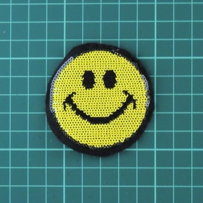 Adesivo bordado sorridente amarelo sobre superfície verde quadriculada