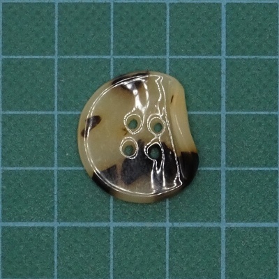 Botão redondo bege e castanho com quatro furos sobre superfície verde de grade azul