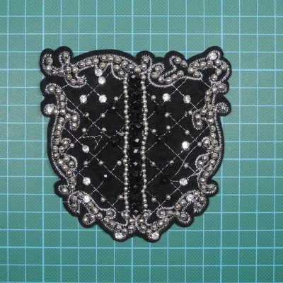 Applique preta com contas prateadas sobre fundo verde quadriculado