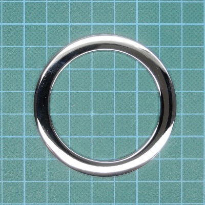 Anel metálico prateado sobre superfície verde com grade branca.