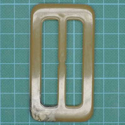 Fivela retangular de plástico bege translúcido sobre fundo verde quadriculado