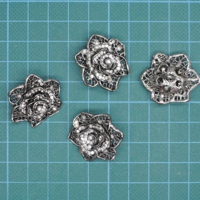 Quatro botões metálicos em forma de flor sobre superfície verde quadriculada