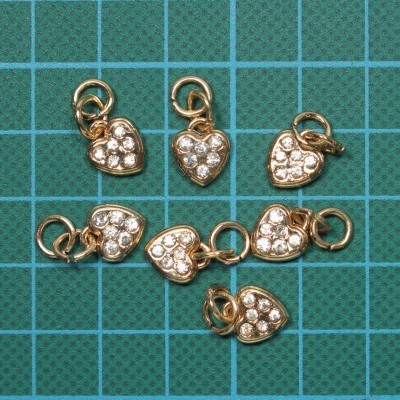 Pendentes em forma de coração dourados com pedras brilhantes sobre fundo verde quadriculado