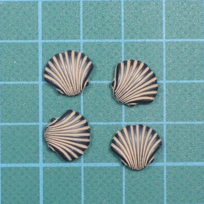 Quatro pequenos pendentes em forma de concha com cores creme e castanho escuro sobre fundo verde com grelha azul