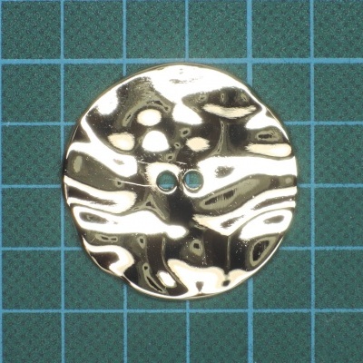 Botão redondo prateado metálico com dois furos sobre superfície quadriculada azul