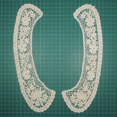 Dois colarinhos de renda branca com padrões florais sobre superfície verde quadriculada