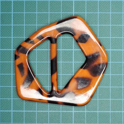 Fivela pentagonal laranja e preta sobre fundo verde quadriculado