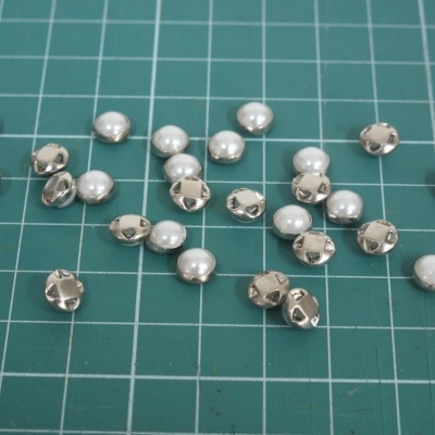 Tachas redondas prateadas e pérolas brancas sobre superfície verde quadriculada