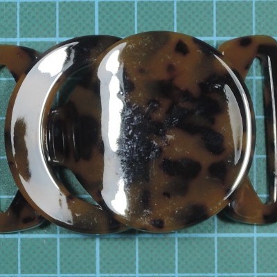 Fivela de plástico marmoreada castanha e preta sobre fundo quadriculado azul