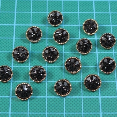 Doze botões redondos facetados pretos com base dourada sobre superfície verde quadriculada.