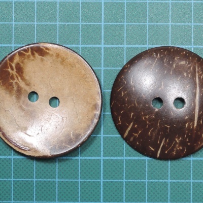 Dois botões redondos de coco com dois orifícios, sobre superfície verde quadriculada.