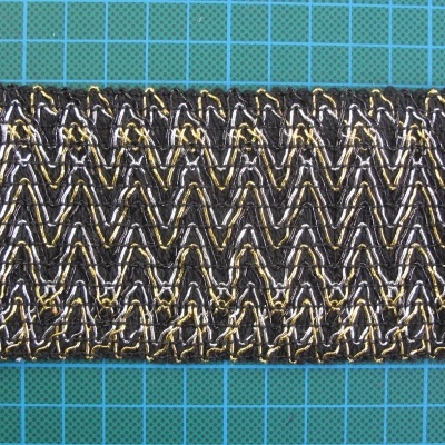 Faixa de tecido trançado em padrão zig-zag preto, dourado e prateado sobre fundo azul quadriculado