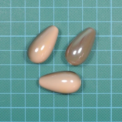 Três contas em forma de gota em tons bege e castanho sobre fundo verde quadriculado