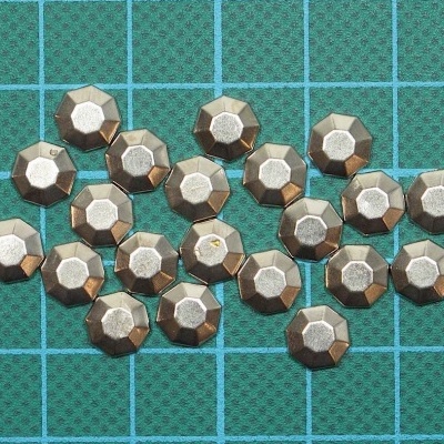 Peças metálicas octogonais prateadas e douradas sobre superfície com grade azul