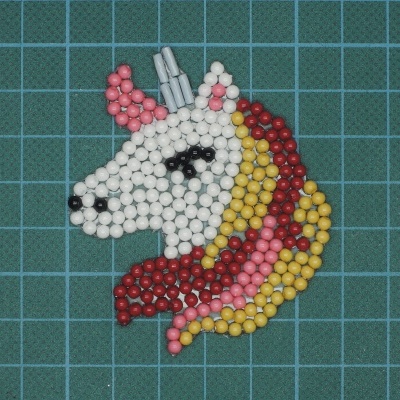 Broche de contas em forma de cabeça de unicórnio colorido sobre fundo quadriculado azul