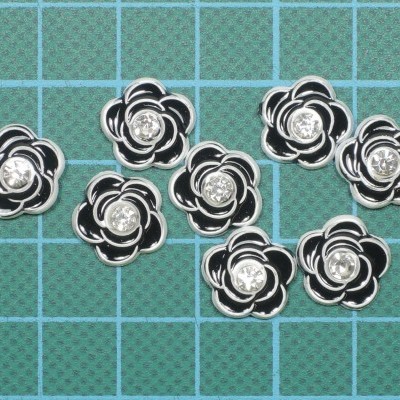 Botões decorativos em forma de flor preto e branco com centro brilhante sobre superfície de corte verde