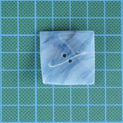 Botão quadrado azul e branco com dois furos sobre superfície azul de cortiça com grelha