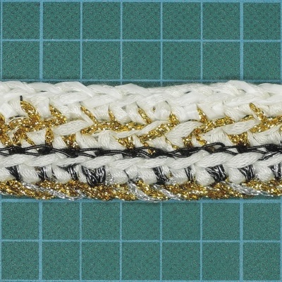 Fita trançada dourada, preta e branca sobre base verde quadriculada