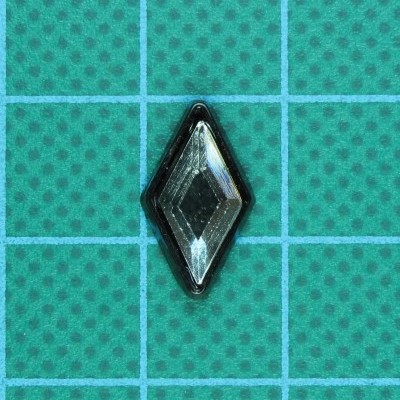 Botão losango transparente com borda preta sobre fundo verde com padrão quadriculado